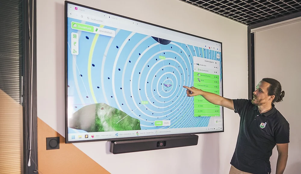 Présentation d'un outil web sur grand écran : vue en plan avec cercles concentriques et panneau des objets de la scène